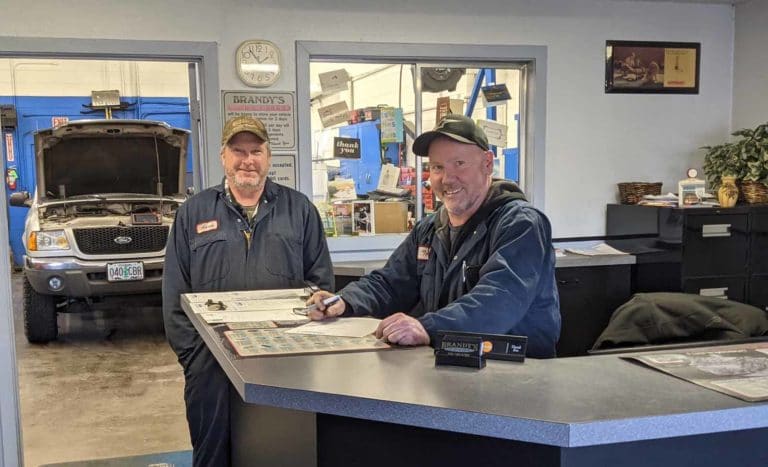 About Brandy's Automotive. Bend, Oregon. Truck and car repair.Brandy and technician smile at camera while working on paperwork in office area