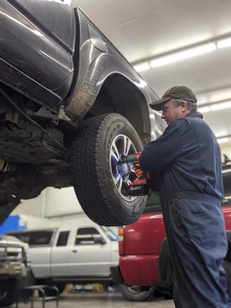 Brandy's Automotive. Bend, Oregon. Truck and car repair.A truck is on a lift so the wheel is at chest height. An employee is using a tool to work on the wheel.