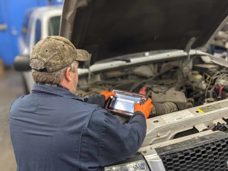 Technician uses a tablet in garage bay as he works on truck engine. Brandy's Automotive. Bend, Oregon. Truck and car repair.