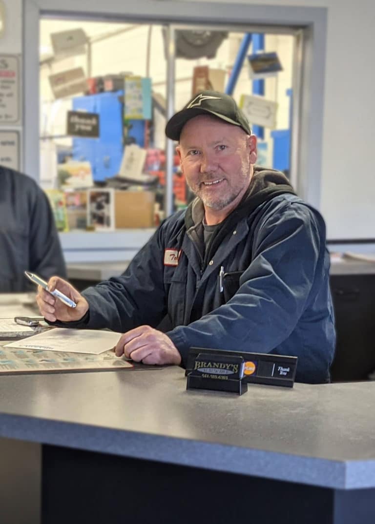 FAQ Tom Brandy (Owner) smiling behind counter. Brandy's Automotive. Bend, Oregon.